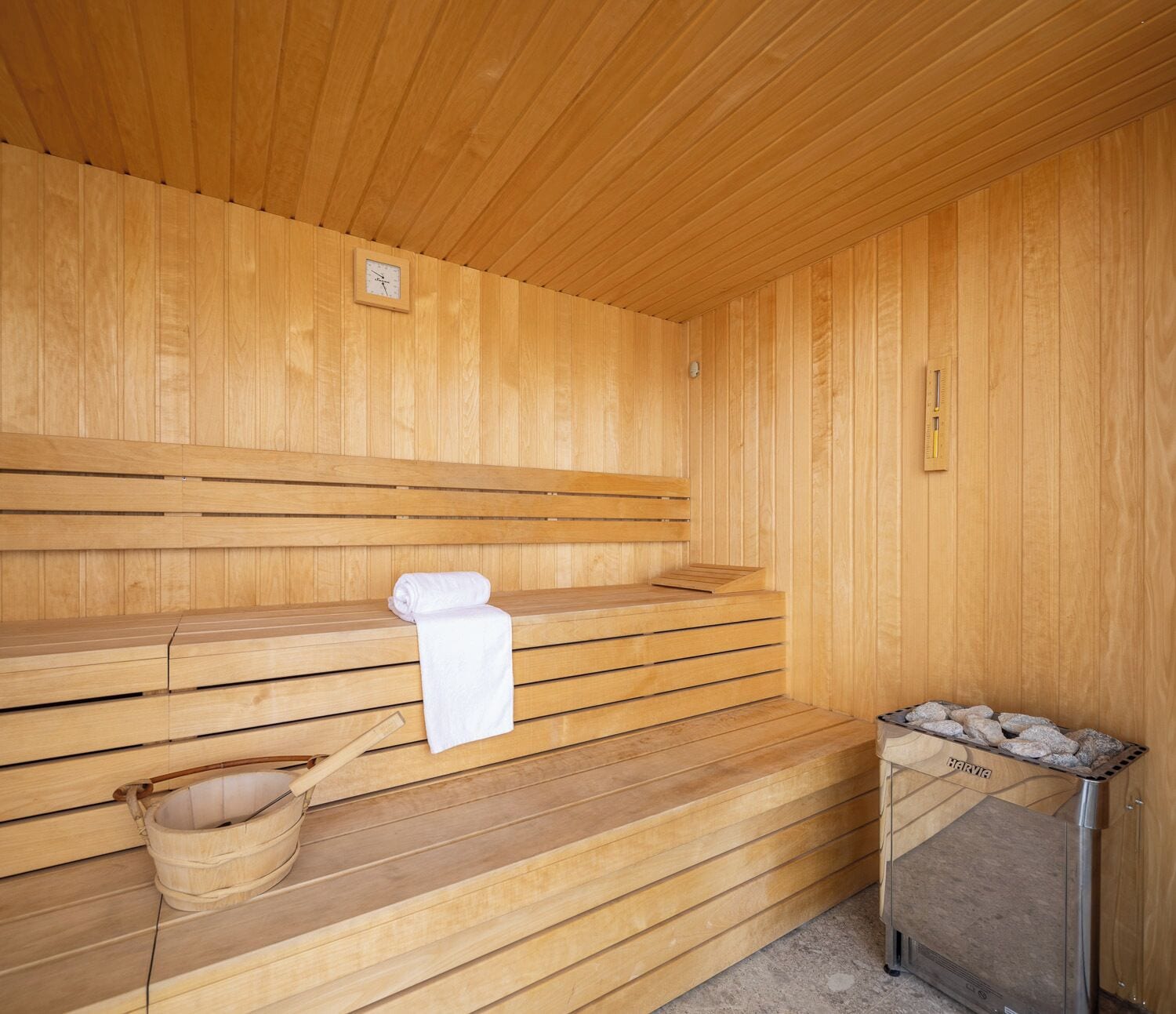 Eine Sauna mit hölzernen Bänken, einem weißen Handtuch, einem Holzwaschbecken und einem Steinkamin.