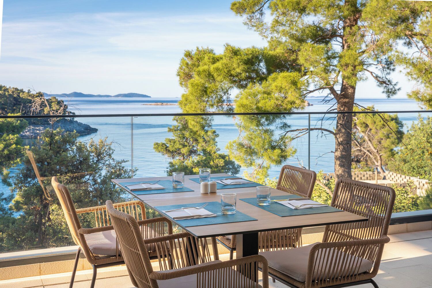 A dining table set for four with chairs, overlooking a body of water and a distant island.