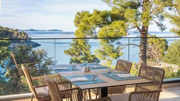 A dining table set for four with chairs, overlooking a body of water and a distant island.
