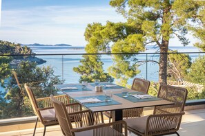 A dining table set for four with chairs, overlooking a body of water and a distant island. - Aminess Alfir Hotel (Blato)
