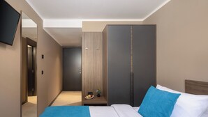 A hotel room with a bed, a wardrobe, a television, and a small table with a vase and fruit. - Aminess Alfir Hotel (Blato)