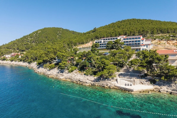 Un hôtel situé sur la côte, avec plusieurs étages, un rivage rocheux et, en arrière-plan, des collines verdoyantes.