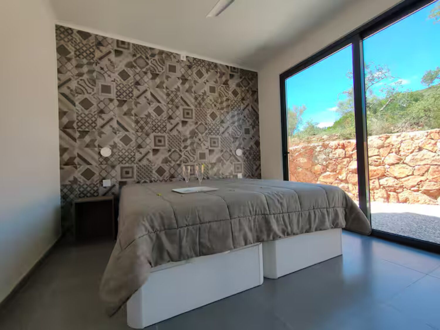 A modern bedroom with a patterned wall, a large window, and a bed with storage drawers.
