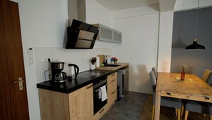 A compact kitchen with wooden cabinets, a built-in oven, a coffee maker, and a microwave. - Elbphilharmonie Suite (Hamburg)