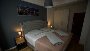 A neatly made bed with a headboard, two bedside tables with lamps, a cityscape painting on the wall, and a wardrobe. - Elbphilharmonie Suite (Hamburg)