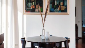 A dining area with a round table, two framed paintings, and a vase with tall grasses.