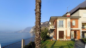 A coastal house with a balcony, a view of the sea, and a mountain in the background.