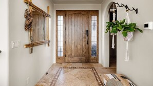 A hallway with a wooden door, a mirror, a macrame plant hanger, and a patterned rug.