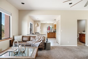 A spacious living room with a glass coffee table, a sofa, and a kitchen in the background.