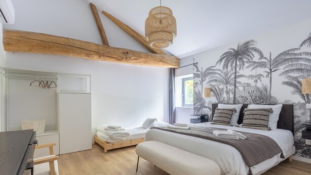 A bedroom with a bed, a desk, a chair, and a hanging light fixture.