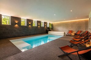 A modern indoor pool area with a rectangular pool, dark walls, and multiple windows. - Renovated, spacious and comfortable 26-bed mill (Saint-Ignat)
