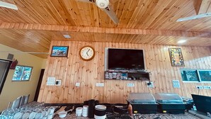 A wooden-paneled room with a ceiling fan, a clock, a flat-screen TV, and a wall-mounted shelf with various items.