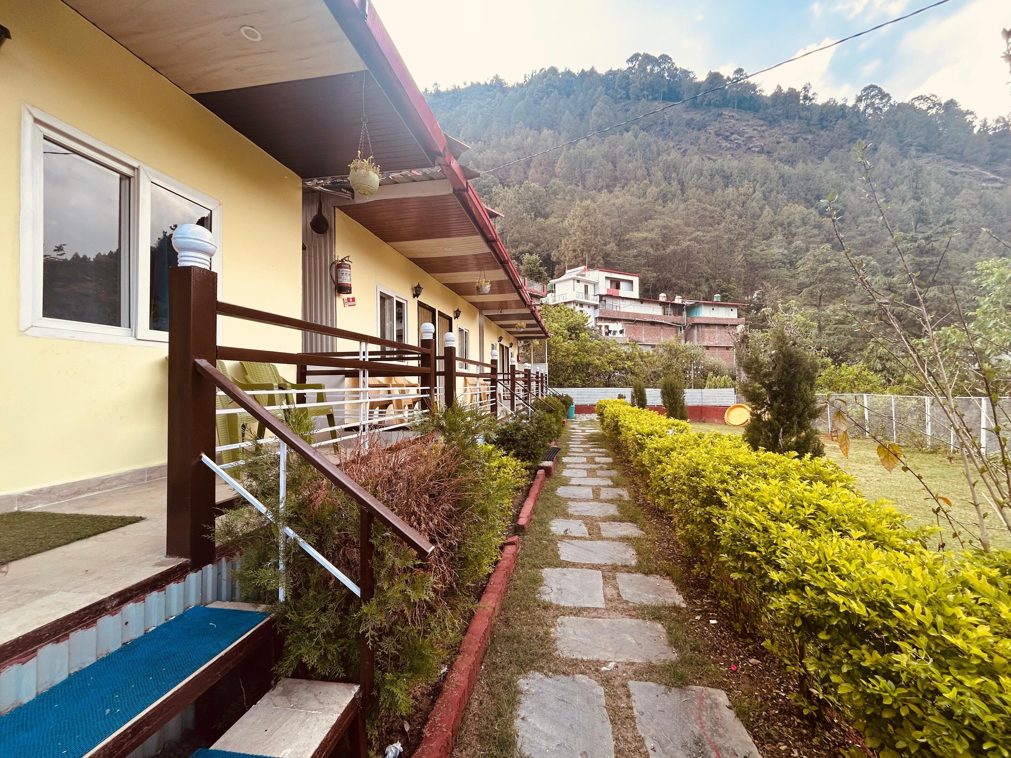 A hotel with a stone pathway leading to a staircase, surrounded by greenery and a mountainous backdrop.