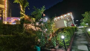 A pathway leading to a building with string lights and a well-maintained garden. - The Pines Mountain View (Ukhimath)