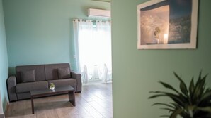 Ein Wohnzimmer mit grauem Sofa, einem kleinen Tisch mit Pflanze und einem gerahmten Bild an der Wand.
