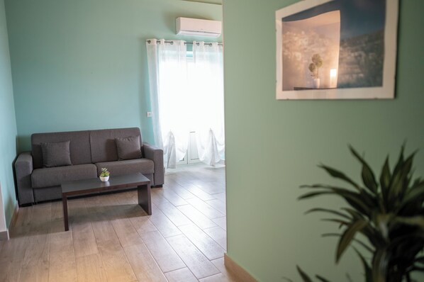 A living room with a grey sofa, a small table with a plant, and a framed picture on the wall.
