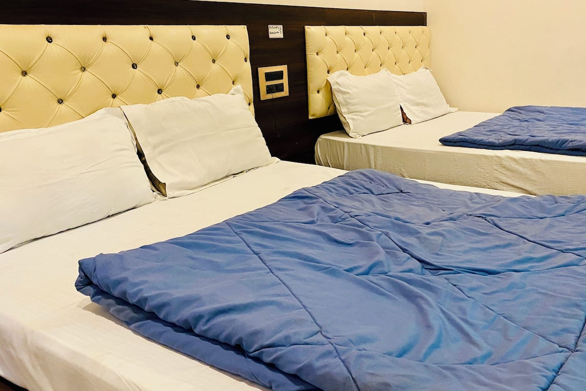 A hotel room with two beds, each with a blue comforter and white pillows. The headboards are tufted and upholstered in a light color.