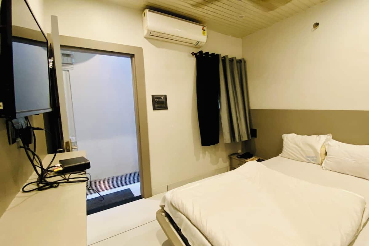A hotel room with a bed, a desk with a computer, an air conditioner, and a door leading to a balcony.
