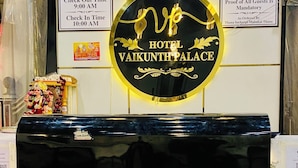 Un mostrador de recepción con encimera de mármol negro, un cartel que dice "HOTEL VAIKUNTH PALACE" y un letrero que indica los horarios de salida y llegada.