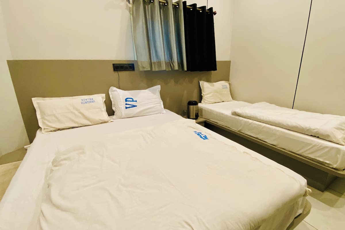 A hotel room with a large bed, two smaller beds, a nightstand, and a power outlet.