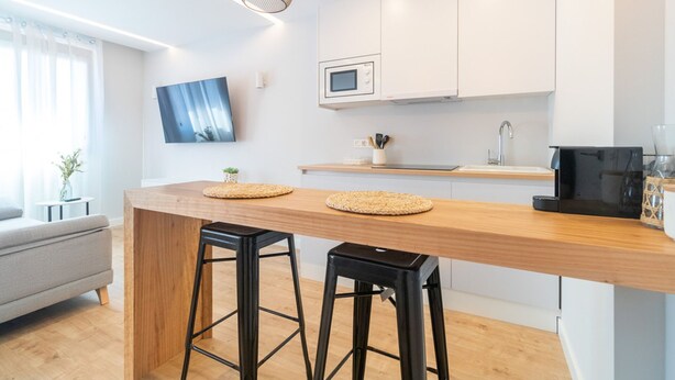 Une cuisine moderne avec un îlot central en bois, deux tabourets de bar, un four à micro-ondes et une machine à café.