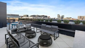A rooftop terrace with outdoor seating, a view of the city skyline, and a modern building in the background.