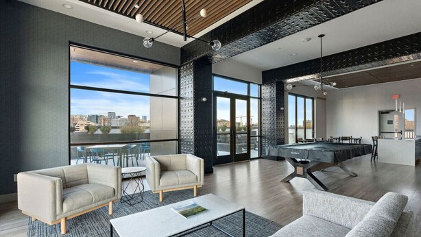 A spacious office with a pool table, comfortable seating, and large windows offering a city view.
