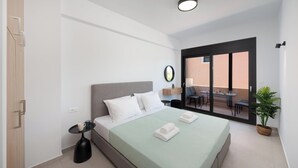 Een moderne hotelkamer met een bed, een klein tafeltje met een kopje, een potplant en een balkon met een tafel en stoelen.