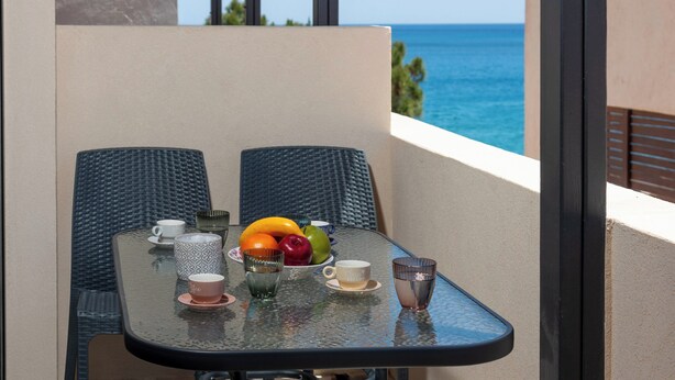 Een balkon met een tafel gedekt voor twee personen, met een schaal fruit, kopjes en een glas.