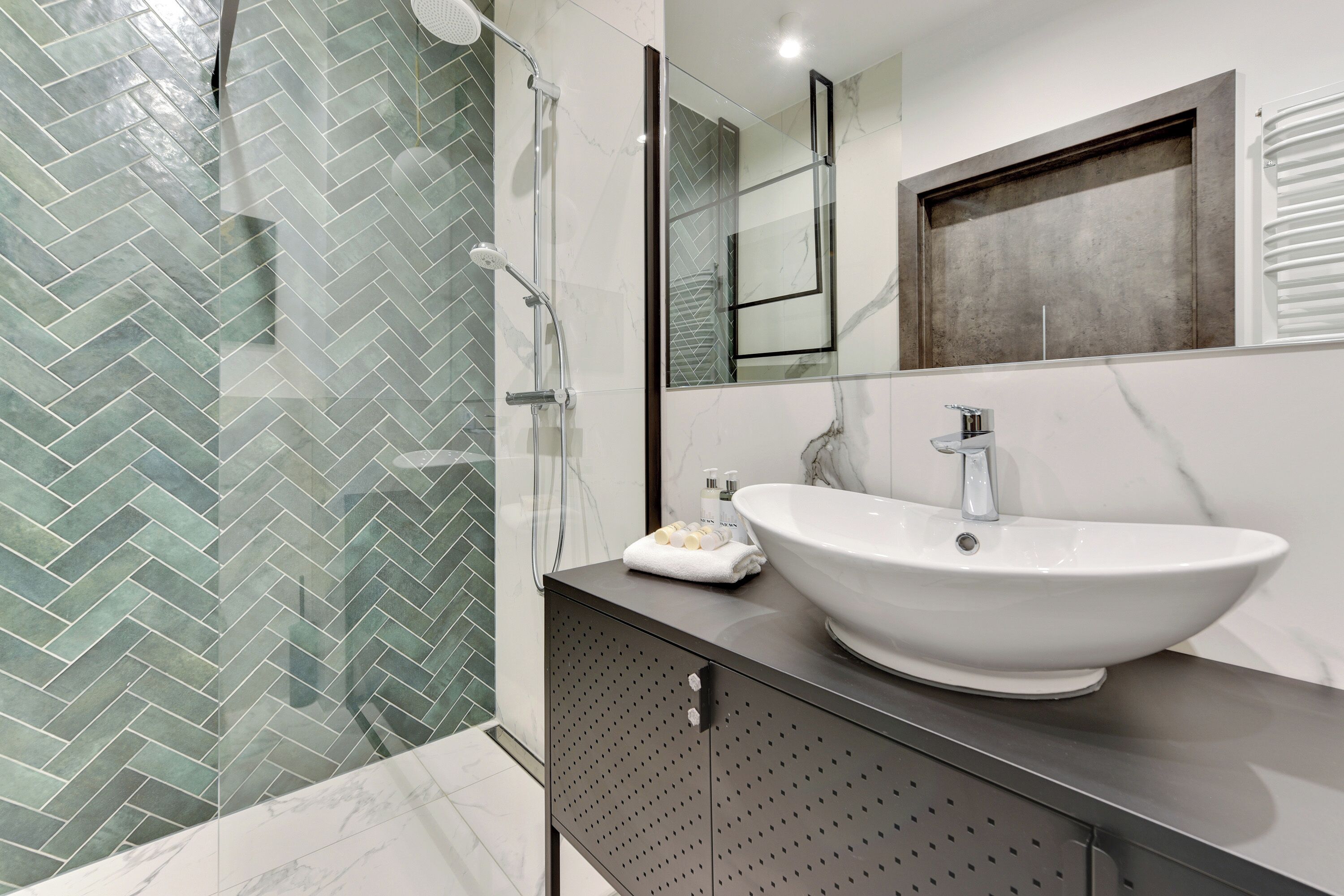 A modern bathroom with a large white sink, a glass shower enclosure, and a herringbone tile pattern on the floor.
