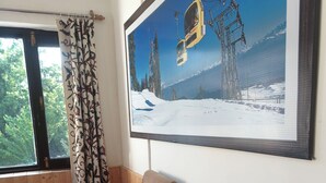 A room with wooden walls, a window with a curtain, and a large framed picture of a ski lift. - Hotel Garden INN (Srinagar)