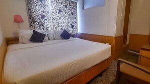 A hotel room with a bed, a desk, a chair, a lamp, and a patterned curtain. - Hotel Garden INN (Srinagar)