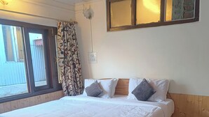 A neatly made bed with a wooden headboard, a patterned curtain, and a ceiling fan. - Hotel Garden INN (Srinagar)