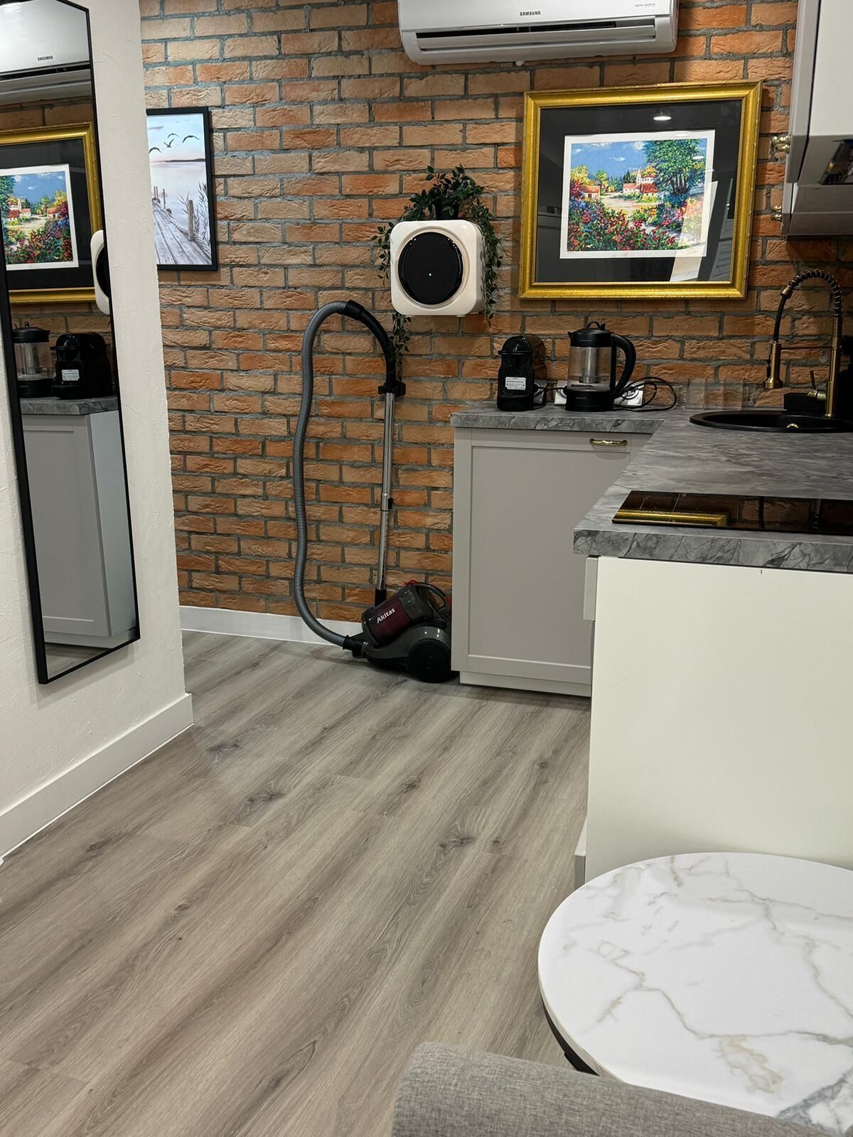 Eine Küche mit Backsteinwand, Staubsauger, Kaffeemaschine und gerahmten Bildern an der Wand.