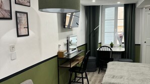 Una habitación de hotel moderna con cama, escritorio con computadora, silla, sofá y una ventana grande con cortinas.