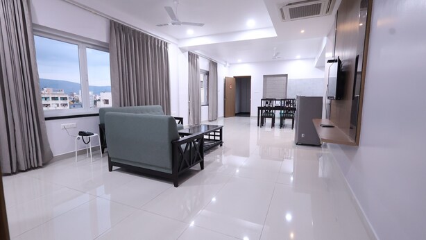 A modern hotel room with a sofa, a dining table, and a TV. - Tirupati Prime Homestay (Tirupati)