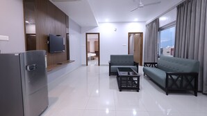 A modern living room with a flat-screen TV, a sofa, a coffee table, and a refrigerator. - Tirupati Prime Homestay (Tirupati)
