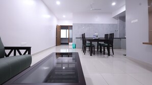 A modern living room with a glass coffee table, a sofa, and a dining area with chairs and a table. - Tirupati Prime Homestay (Tirupati)