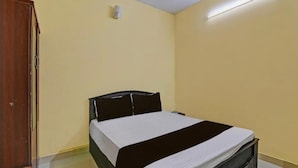 Una habitación pequeña con cama individual, un armario de madera, una mesita de noche y una lámpara fijada a la pared.