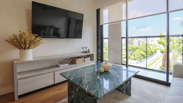 A modern living room with a large TV, a marble coffee table, and a view of a cityscape through large windows. - w* | Cozy 1BR w/ Balcony in San Isidro (Lima)