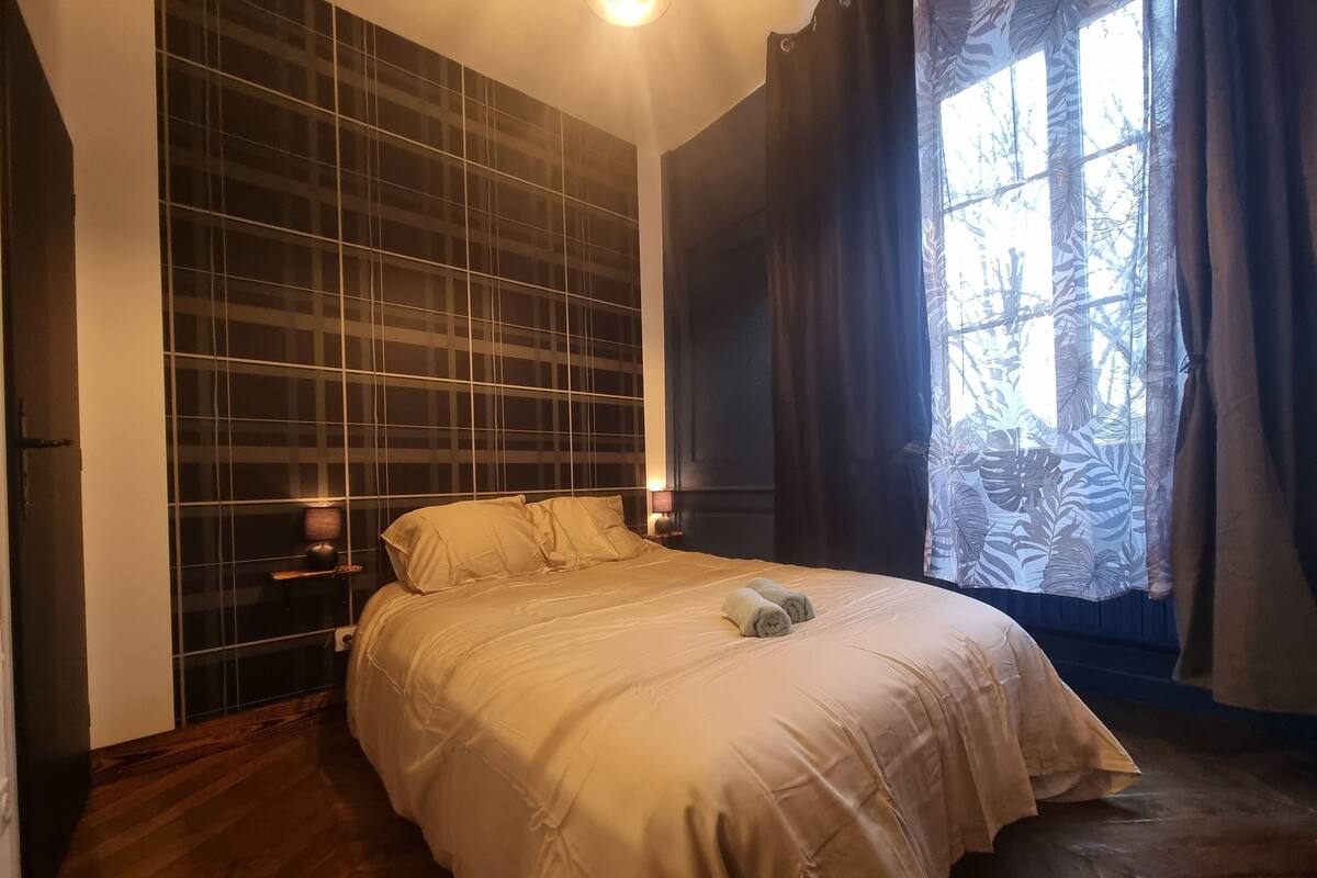 A bedroom with a large bed, a window with curtains, and a wall with a grid pattern.