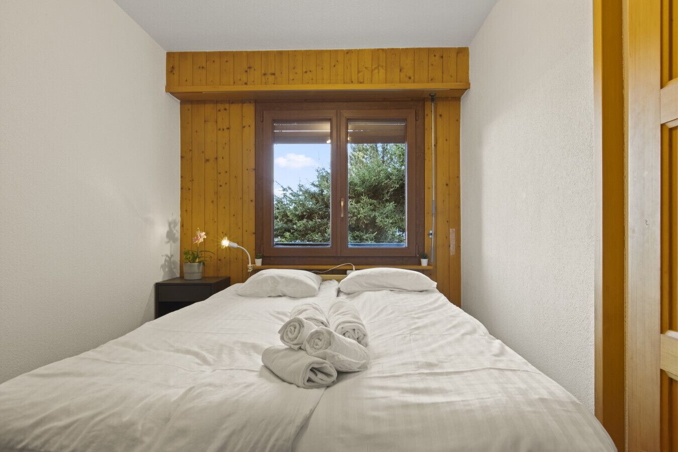 Quarto com uma cama, duas janelas, uma mesa de cabeceira e um abajur.