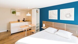 Un dormitorio moderno con una cama grande, un escritorio y una silla. Una pared azul con dos obras de arte enmarcadas.