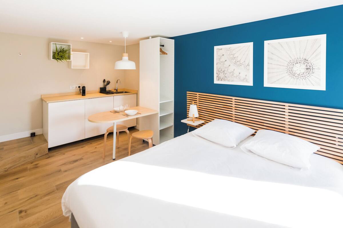 A modern bedroom with a large bed, a desk, and a chair. There is a blue wall with two framed artworks.