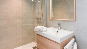 Un baño moderno con cabina de ducha de vidrio, lavamanos blanco y tocador de madera.