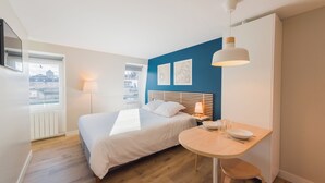 Un dormitorio con cama, mesita de noche, lámpara y vistas a la ciudad a través de una ventana.