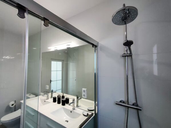 A modern bathroom with a glass shower enclosure, a large mirror, and a white sink.