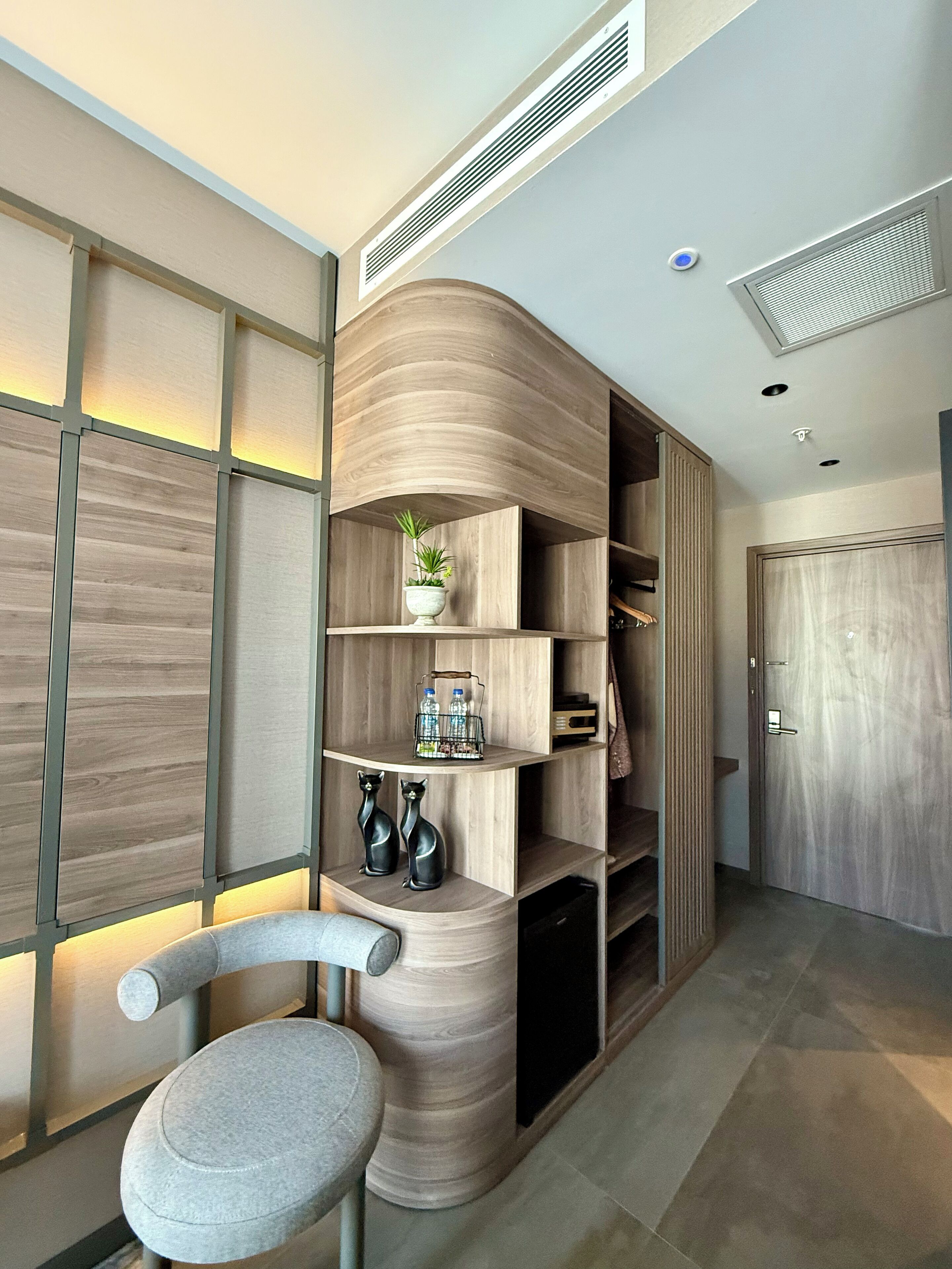 A modern interior with a curved wooden shelving unit, a grey upholstered chair, and a door with a metallic handle.