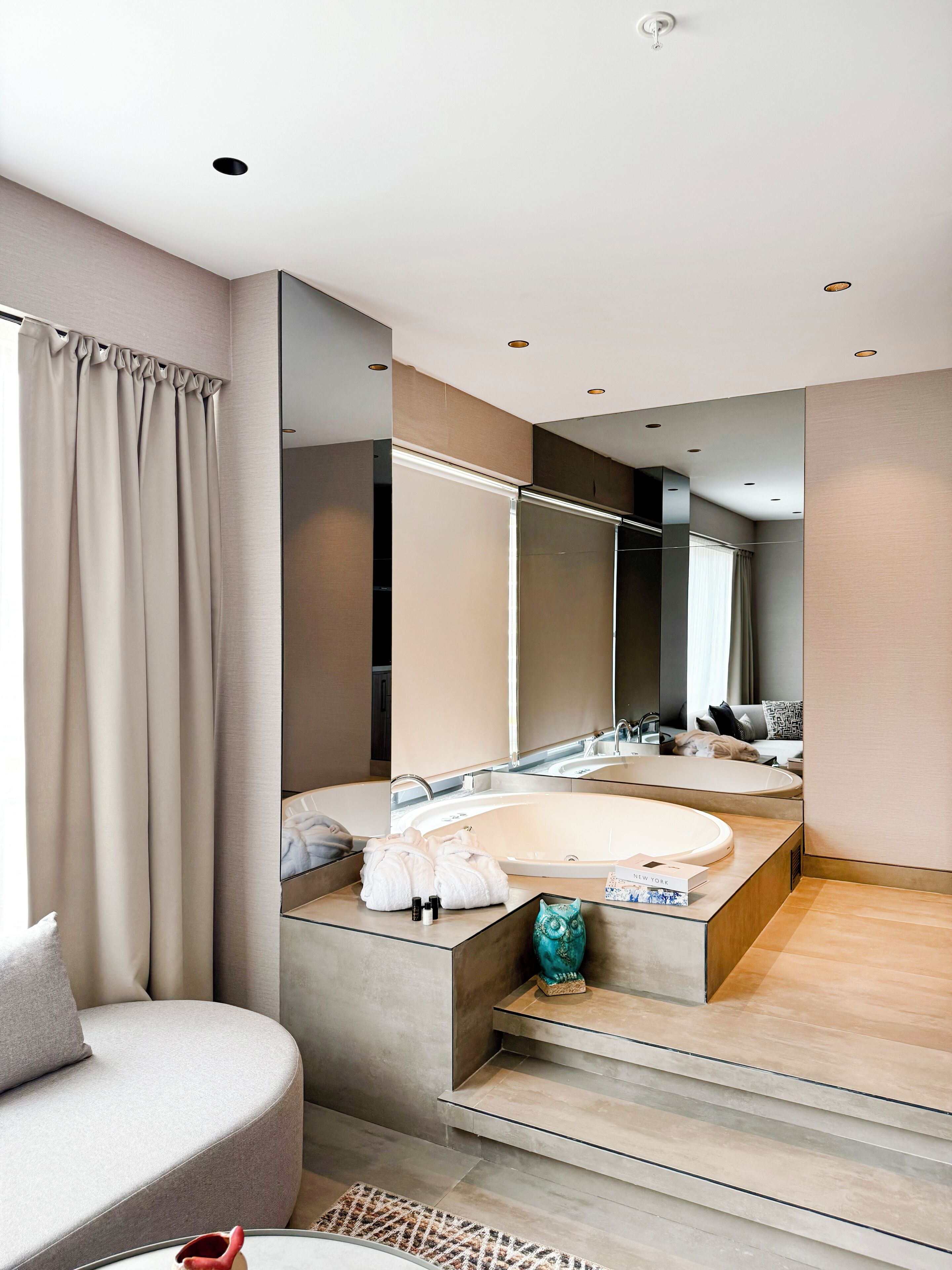 A modern bathroom with a large bathtub, a vanity with a mirror, and a seating area with a sofa.