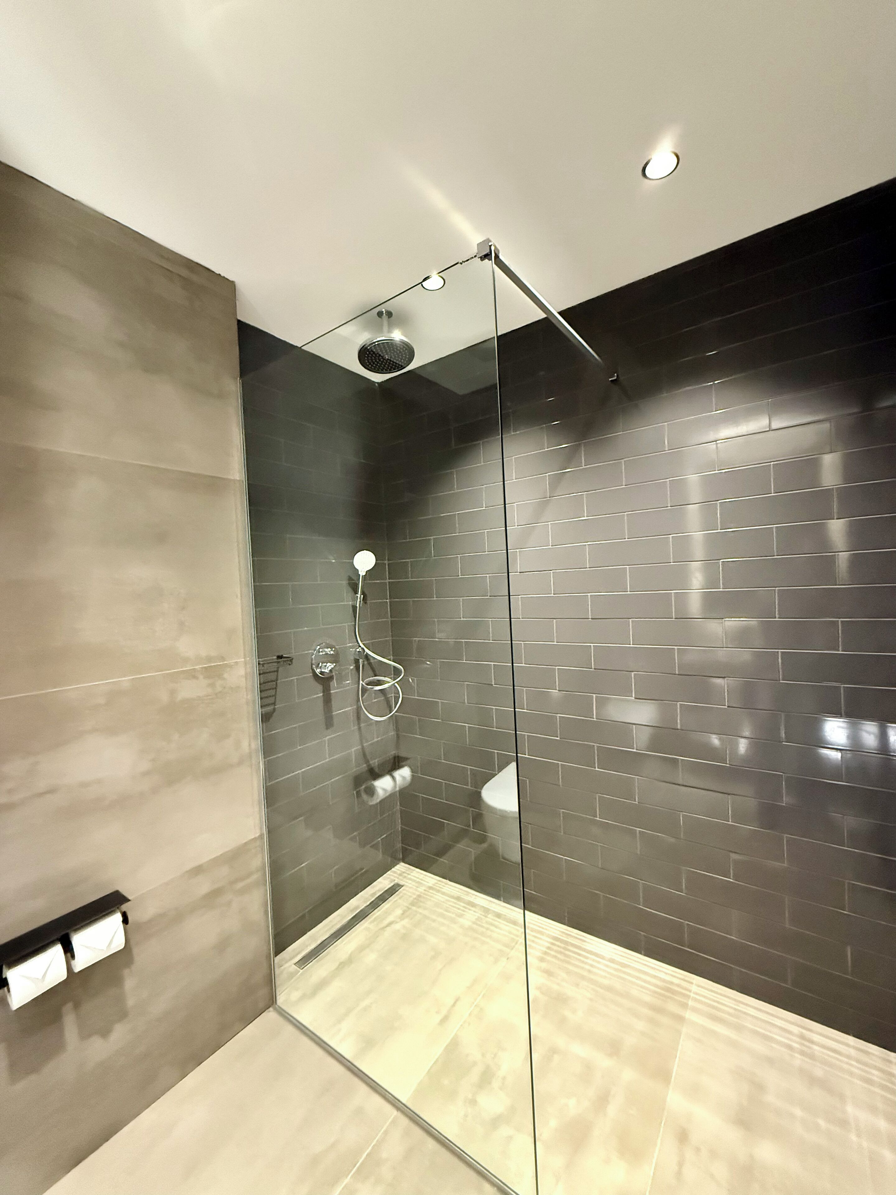 A modern shower with a glass door, a dark tiled wall, and a light-colored floor.